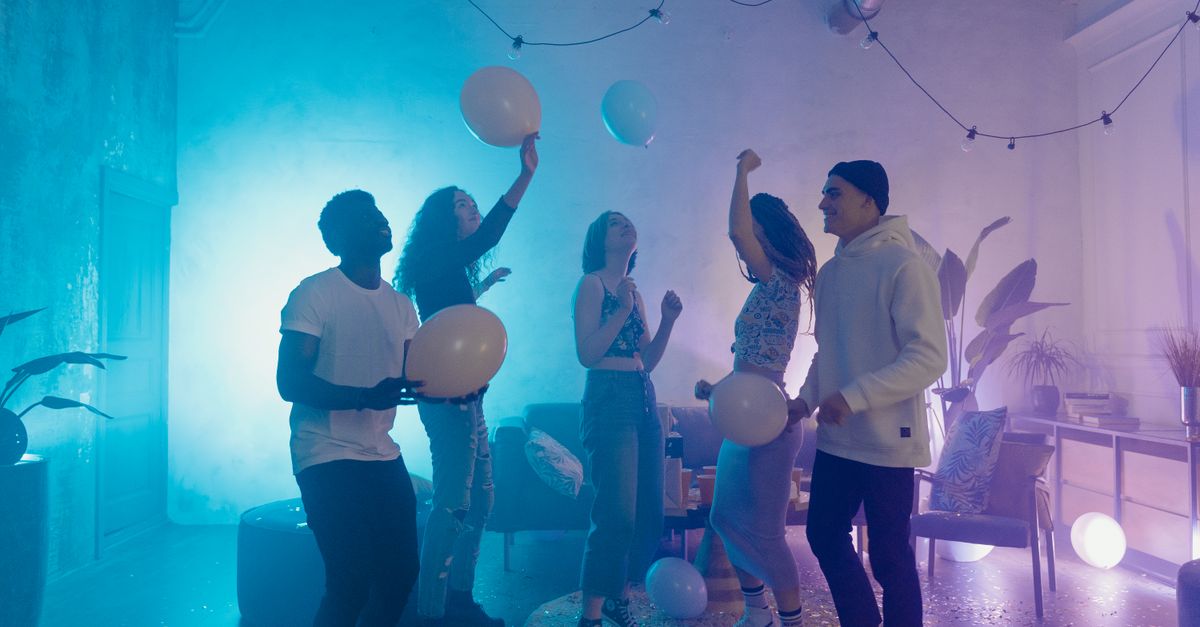 A lively indoor party scene with diverse friends celebrating with balloons and colorful lights.